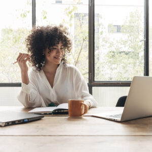 Smiling, happy, Young beautiful african american woman studying at home with laptop. Taking notes in notebook. Bright spacious living room. E-learning concept. Study at home concept.