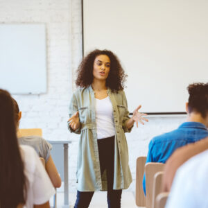 Female student gesturing while explaining during presentation. Young woman is giving speech in classroom. She is sharing ideas with classmates.